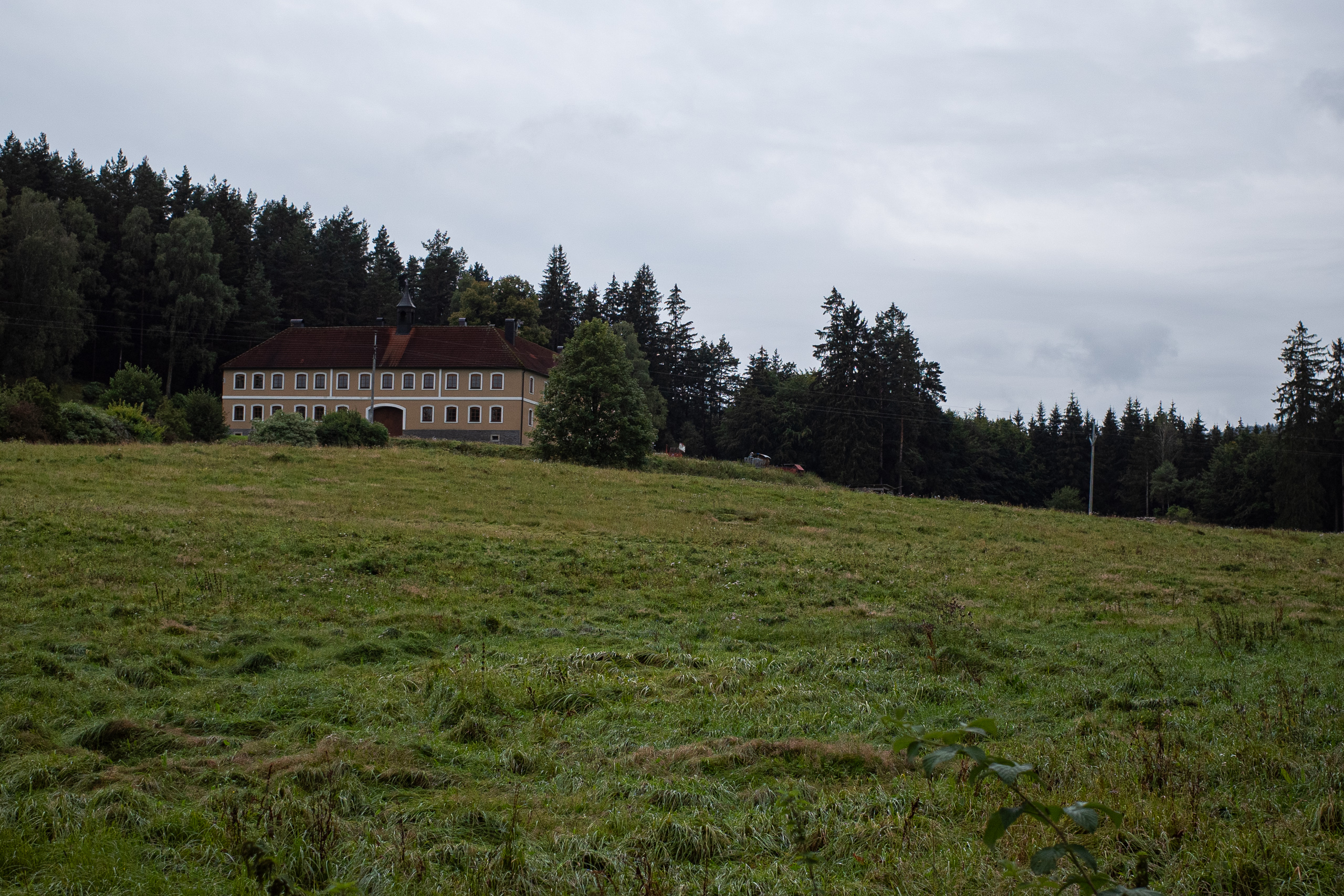 Langgestrecktes Gutsgebäude mit Dachreiter über der nassen Wiese
